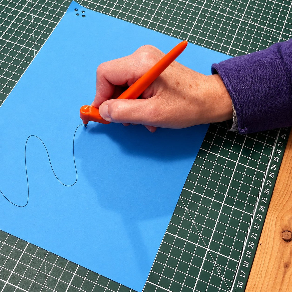 Main qui trace une ligne ondulée sur du carton bleu avec le Gyro-Cut PRO, étape 1