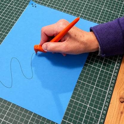Main qui trace une ligne ondulée sur du carton bleu avec le Gyro-Cut PRO, étape 1