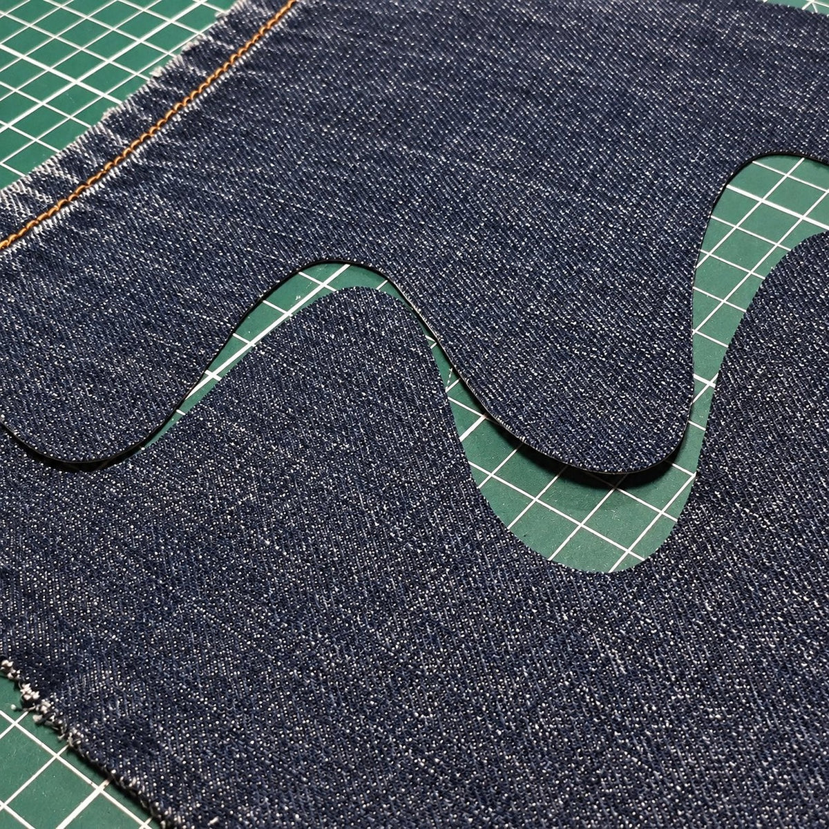Vraie coupe : une vague nette découpée dans du jean, sur un tapis de coupe