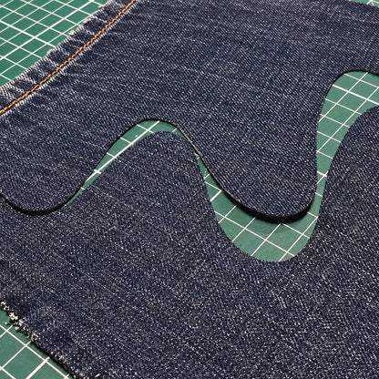 Vraie coupe : une vague nette découpée dans du jean, sur un tapis de coupe